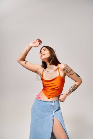 Photo for A young woman with brunette hair wearing an orange top and blue skirt twirls in a vibrant studio setting. - Royalty Free Image