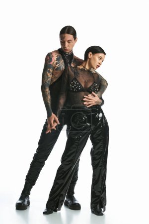 A young tattooed couple waltzing gracefully in a studio against a grey background.