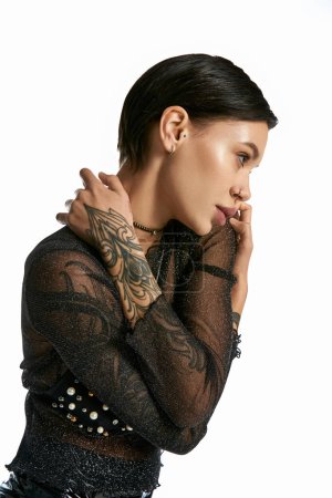 Una joven con un tatuaje llamativo adornando su brazo, de pie en un estudio con su pareja sobre un fondo gris.
