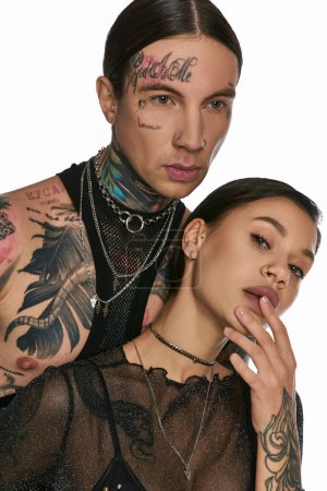 Téléchargez les photos : Un jeune homme et une jeune femme avec des tatouages complexes sur le visage posent dans un studio sur fond gris. - en image libre de droit