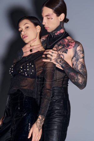 Foto de Una joven pareja tatuada de pie juntos en un estudio sobre un fondo gris. - Imagen libre de derechos