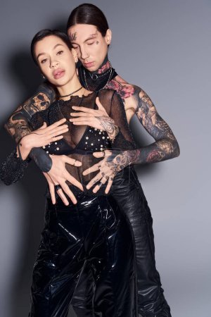 Téléchargez les photos : Couple tatoué se tiennent en confiance côte à côte dans un studio sur un fond gris. - en image libre de droit