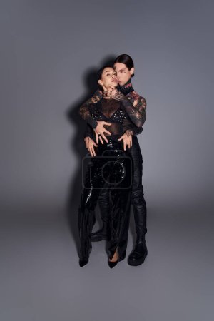 Téléchargez les photos : Un jeune homme et une jeune femme tatoués posant ensemble dans un studio sur fond gris. - en image libre de droit