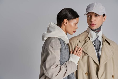 Téléchargez les photos : A young man and woman wearing trench coats stand next to each other in a studio against a grey background. - en image libre de droit