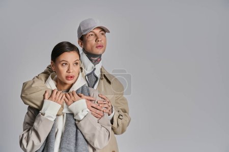 Téléchargez les photos : Un jeune homme et une jeune femme élégants portant des trench-coats se tiennent côte à côte dans un studio sur un fond gris. - en image libre de droit