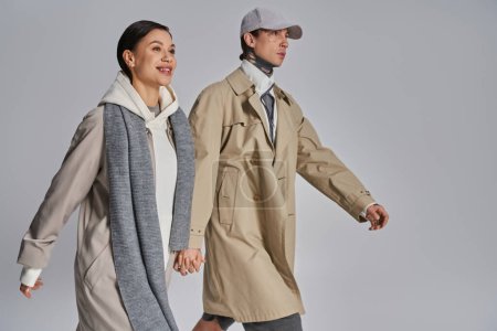 Photo for Young stylish couple in trench coats walking together in a studio against a grey background. - Royalty Free Image