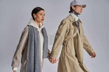 A young stylish couple in trench coats walking hand in hand, immersed in a moment of connection and love.