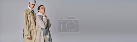 Téléchargez les photos : Un jeune homme et une jeune femme, élégamment vêtus de trench coats, debout l'un à côté de l'autre dans un studio sur fond gris. - en image libre de droit