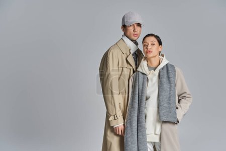 Téléchargez les photos : Un jeune couple élégant se tient côte à côte en trench-coat sur fond de studio gris. - en image libre de droit