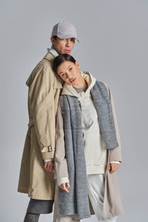 Foto de Un joven hombre y una mujer se paran elegantemente uno al lado del otro en abrigos de trinchera, exudando estilo y sofisticación en un entorno de estudio. - Imagen libre de derechos