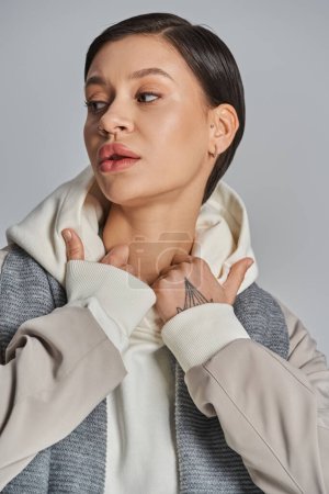 Foto de A young woman exudes elegance in a gray jacket and white shirt against a neutral studio backdrop. - Imagen libre de derechos