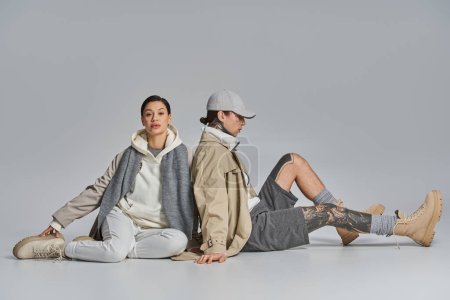 A stylish couple in stylish trench coats sitting together on the ground