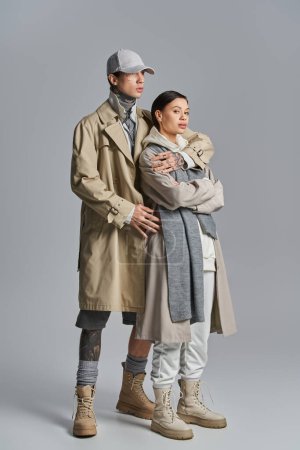 Téléchargez les photos : Un couple élégant, vêtu de trench coats, debout côte à côte dans un studio sur fond gris. - en image libre de droit