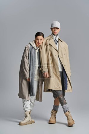 Téléchargez les photos : Un jeune couple élégant se tient côte à côte en trench-coat dans un studio sur fond gris. - en image libre de droit