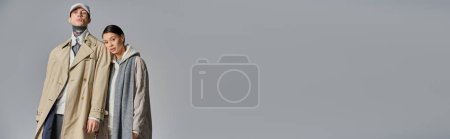 Téléchargez les photos : Couple élégamment vêtus de trench coats se tiennent côte à côte devant une toile de fond gris uni. - en image libre de droit