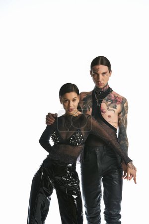 Téléchargez les photos : Un jeune homme et une jeune femme élégants et tatoués se tiennent ensemble dans un studio, mettant en valeur leur look unique et leur connexion. - en image libre de droit