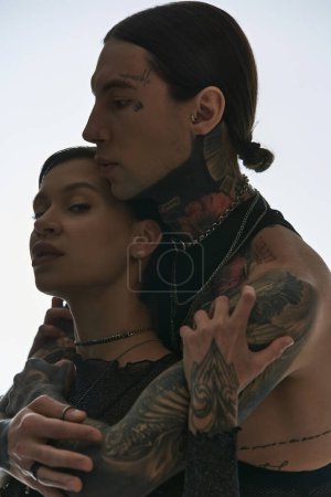 Young, stylish couple with arm tattoos, posing in a studio against a grey background.