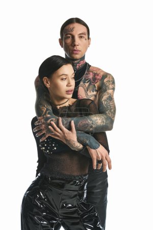 Un jeune couple élégant avec des tatouages complexes sur les bras pose dans un studio sur un fond gris.