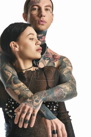 Una pareja joven y elegante con tatuajes en brazos posa en un estudio sobre un fondo gris.