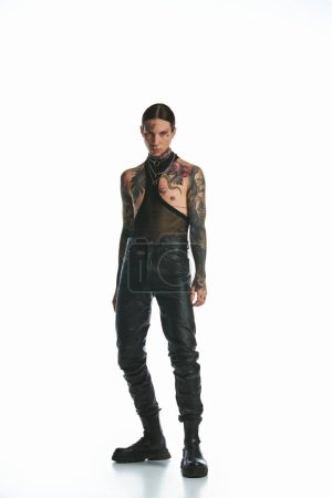 A young man with tattoos confidently stands in front of a white background.