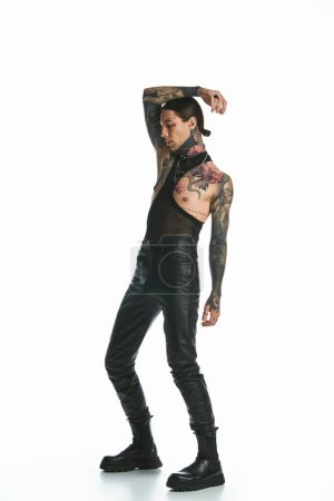 A stylish young man with tattoos stands confidently against a white background.