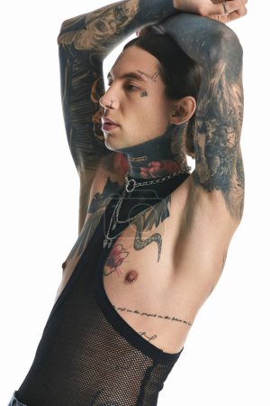 A stylish young man proudly showcases intricate tattoos on his arm and chest, exuding artistic expression and individuality.