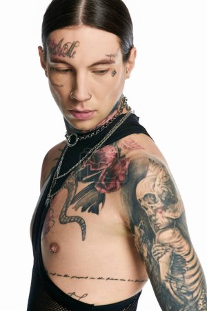 A young stylish man proudly displaying a skeleton tattoo in a studio setting against a grey background.