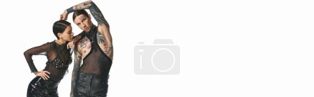 Téléchargez les photos : Un couple jeune, élégant et tatoué debout en toute confiance dans un studio sur fond gris. - en image libre de droit
