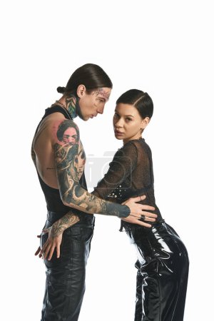 Un jeune homme et une jeune femme élégants ornés de tatouages se tiennent ensemble dans un studio sur un fond gris.