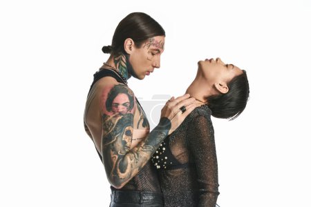 Photo for A young stylish and tattooed couple standing close together in a studio against a grey background. - Royalty Free Image