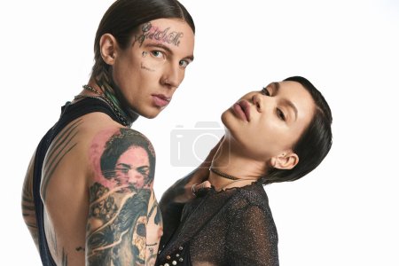 Foto de Una pareja joven y elegante con tatuajes en el brazo abrazándose en un estudio sobre un fondo gris. - Imagen libre de derechos