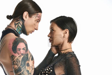 Foto de Una elegante pareja joven con tatuajes parados uno al lado del otro en un estudio sobre un fondo gris. - Imagen libre de derechos