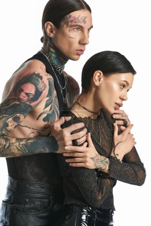 Foto de Una pareja joven y elegante con tatuajes de pie lado a lado en un estudio sobre un fondo gris. - Imagen libre de derechos