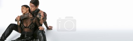 Photo for A young stylish couple with tattoos strike poses in a photo studio against a grey background. - Royalty Free Image