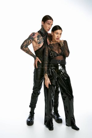 Photo for A young stylish couple with tattoos standing close together in a studio on a grey background. - Royalty Free Image