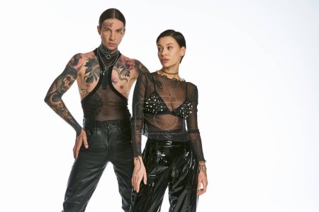 Téléchargez les photos : Un jeune couple élégant et tatoué se tient côte à côte dans un studio sur fond gris. - en image libre de droit