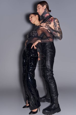 Téléchargez les photos : Un jeune couple élégant en tenue noire avec des tatouages, posant dans un studio sur un fond gris. - en image libre de droit