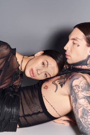 Téléchargez les photos : Un jeune couple élégant et tatoué posant en toute confiance dans un studio sur fond gris. - en image libre de droit