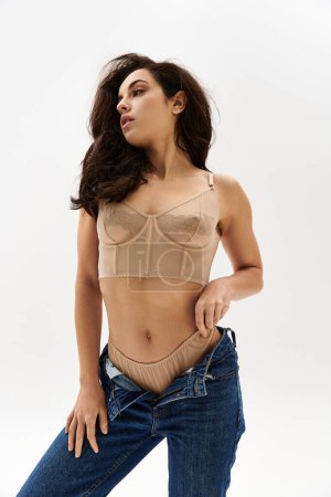A young woman strikes a seductive pose wearing a tan bra top.