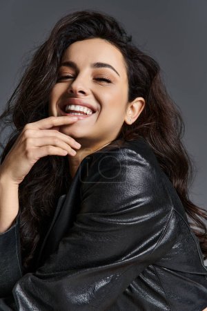 Una mujer sonriente en una chaqueta de cuero negro emana confianza y estilo.