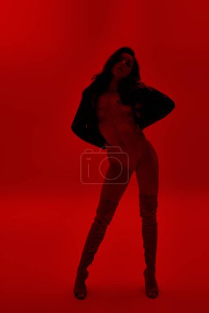 Téléchargez les photos : Jeune femme en lingerie debout en toute confiance dans une salle rouge vibrante avec les mains sur les hanches. - en image libre de droit