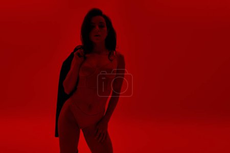 Téléchargez les photos : Femme debout dans une chambre rouge avec une veste sur le dos. - en image libre de droit