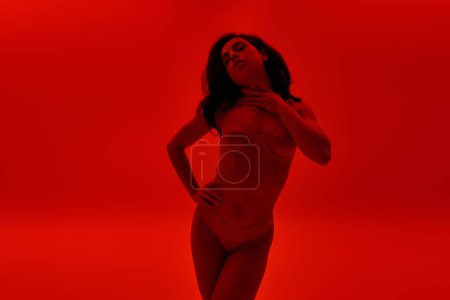 Photo for Young woman confidently stands in lingerie against vibrant red backdrop. - Royalty Free Image