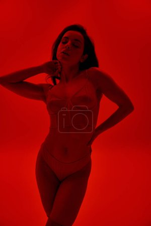A captivating young woman strikes a seductive pose in a fiery red bodysuit.