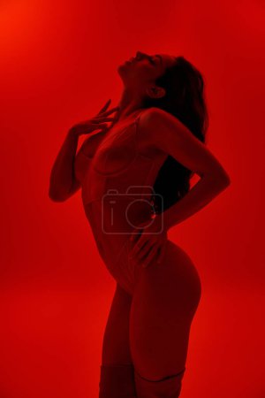 Mujer en lencería golpeando una pose segura con las manos en las caderas en una vibrante habitación roja.