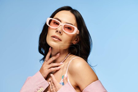 A stylish woman strikes a pose in pink sunglasses against a vibrant blue backdrop in a summer-inspired studio setting.