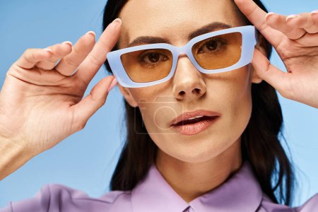 Téléchargez les photos : Une femme à la mode dans une chemise violette et des lunettes de soleil bleues sur un fond bleu vif. - en image libre de droit