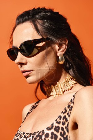 A stylish woman with sunglasses poses in a leopard print top against an orange studio background, exuding summertime fashion vibes.