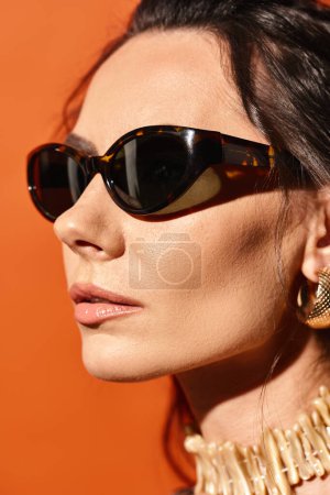 Téléchargez les photos : Une femme à la mode dégage des vibrations estivales avec des lunettes de soleil et un collier en or sur fond orange. - en image libre de droit