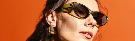 Téléchargez les photos : Une femme élégante portant des lunettes de soleil rondes sur un fond orange respirant les vibrations de la mode estivale. - en image libre de droit